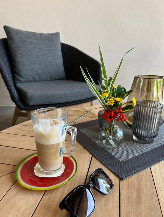 Bistro Tisch mit Sonnenbrille,Kaffee und schöner Deko im Hintergrund ein grauer Sessel